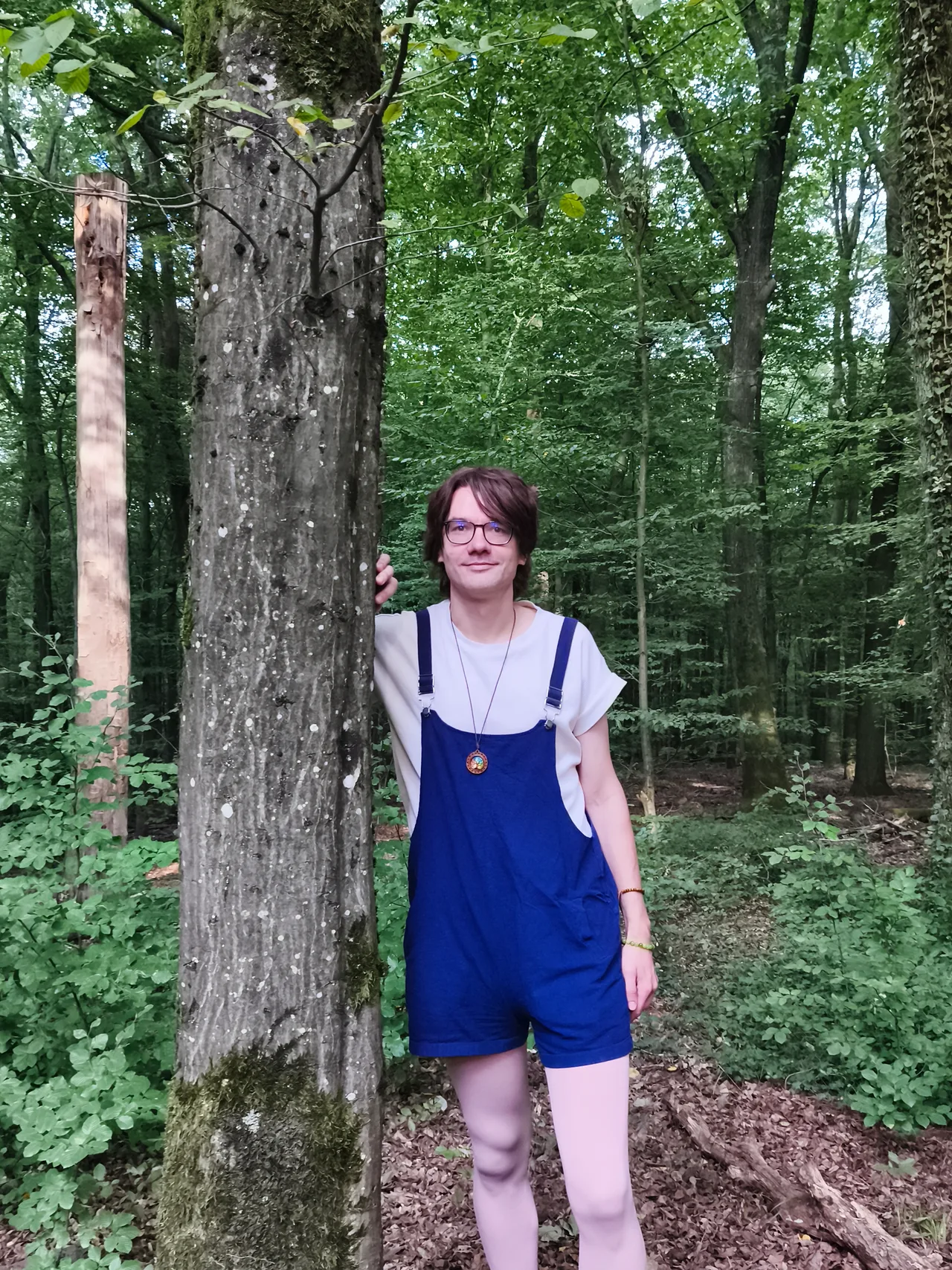 Maik Schneekönig steht neben einem Baum im Wald und lächelt in die Kamera.