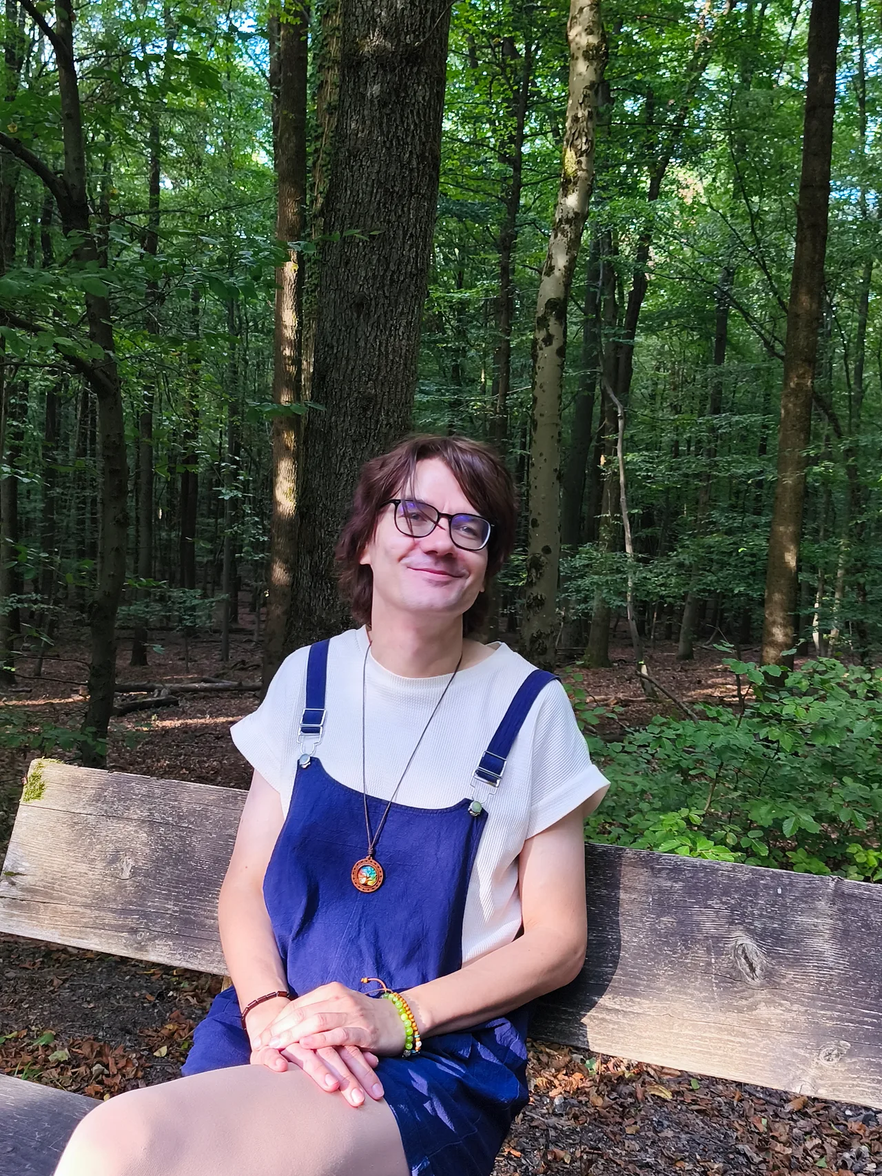 Maik Schneekönig sitzt lächelnd mit aufgelegten Händen auf einer Bank im Wald.
